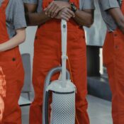 Three workers wearing uniform standing while holding cleaning equipments.