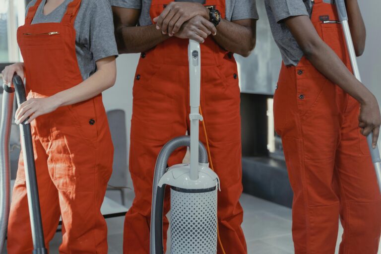 Three workers wearing uniform standing while holding cleaning equipments.