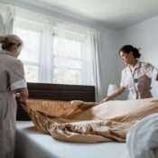 Two female house help setting up the bedsheet.