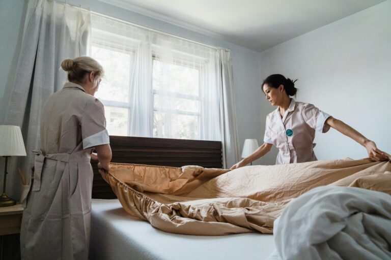 Two female house help setting up the bedsheet.