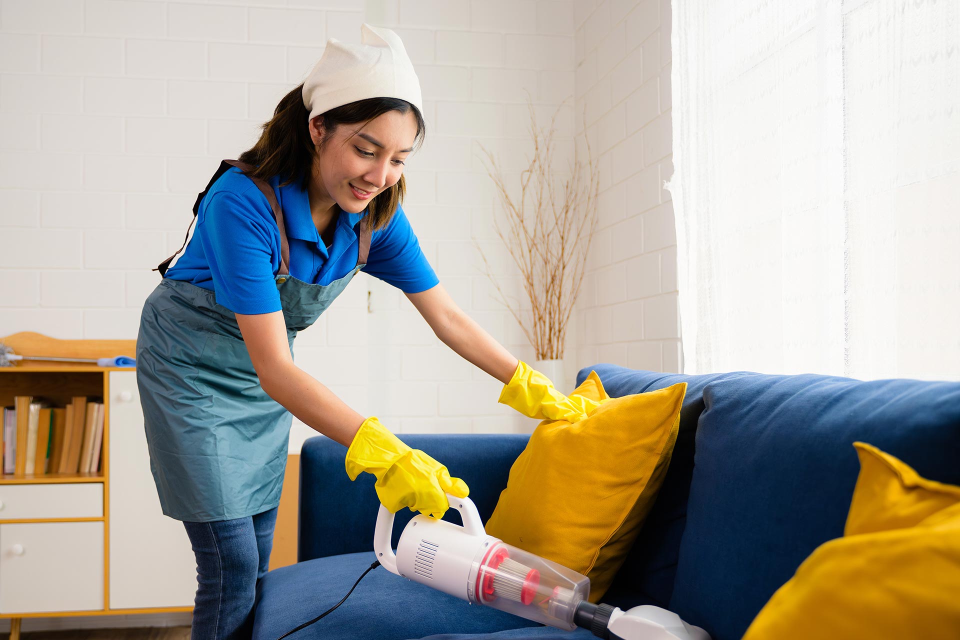 A domestic helper vacuuming the dirt out of sofa.