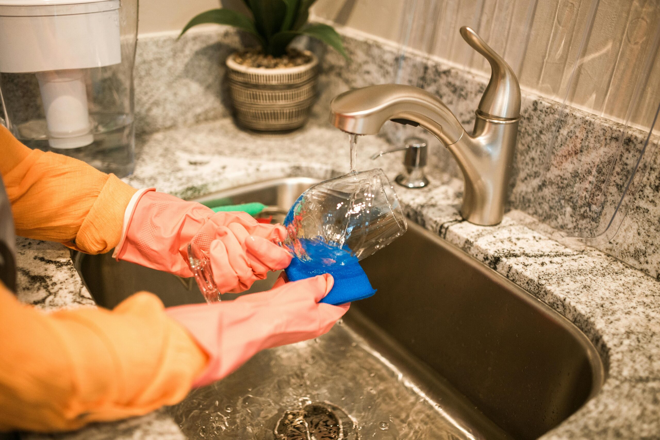 Domestic helper washing a glass at the kitchen sink, highlighting essential household support for busy working families in Singapore.