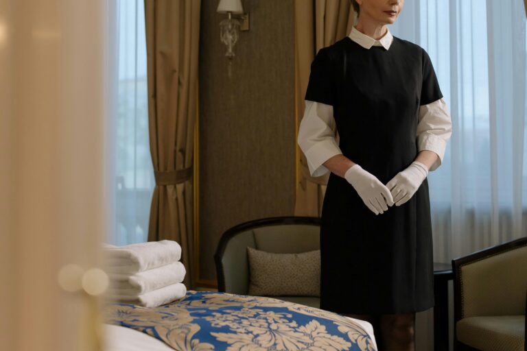 Professional housekeeper in formal uniform standing in a well-prepared hotel room—representing how maid recruitment agencies in Singapore ensure quality and trust.