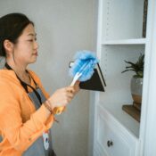 Domestic helper dusting a bookshelf as part of household chores during a performance review process.