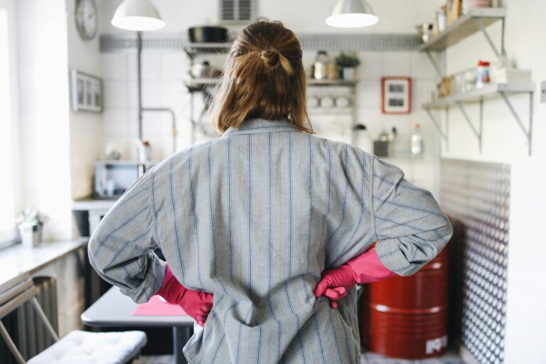 Back view of a woman in cleaning gloves assessing kitchen tasks, symbolizing planning and prioritizing household needs before hiring a domestic helper.