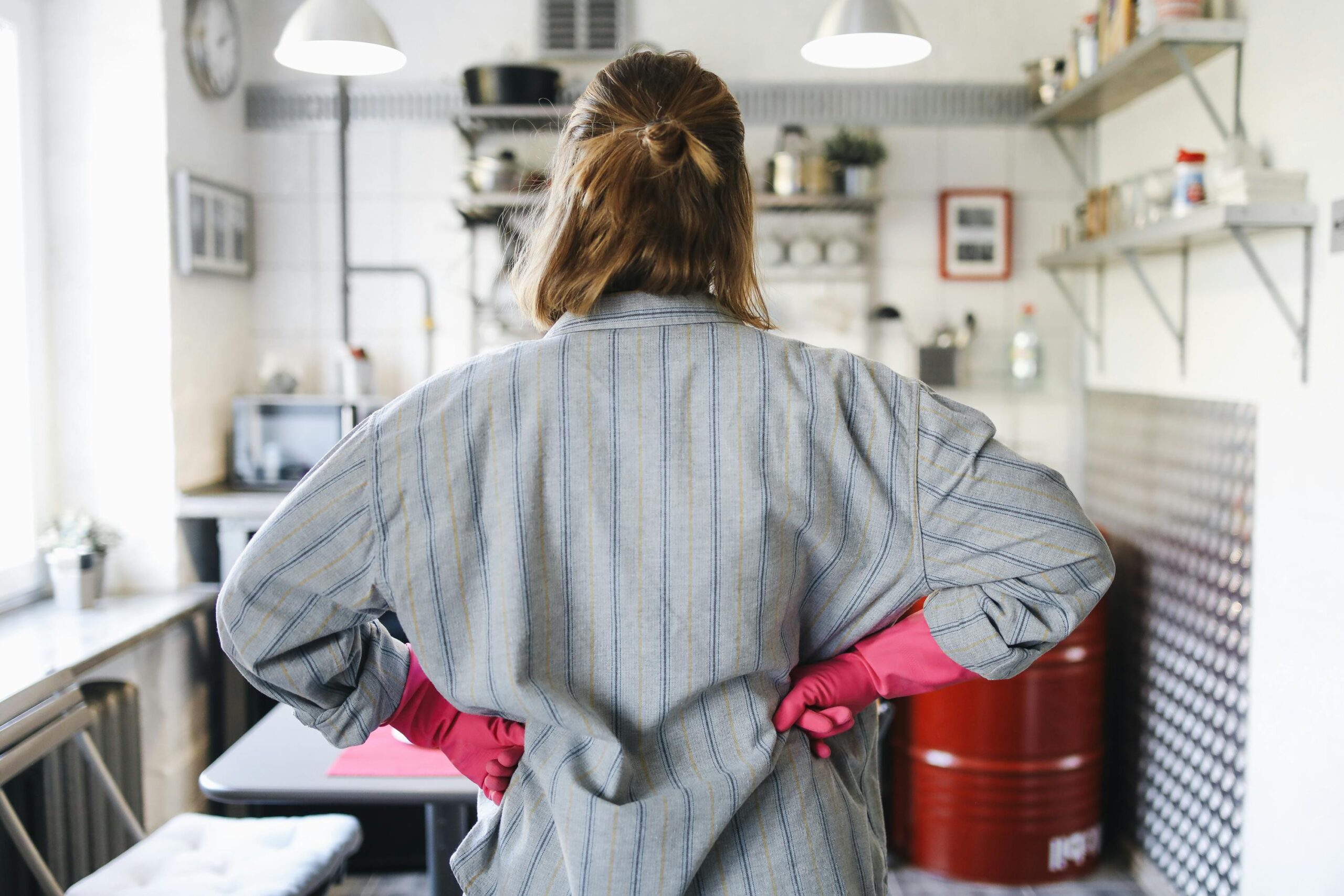 Back view of a woman in cleaning gloves assessing kitchen tasks, symbolizing planning and prioritizing household needs before hiring a domestic helper.