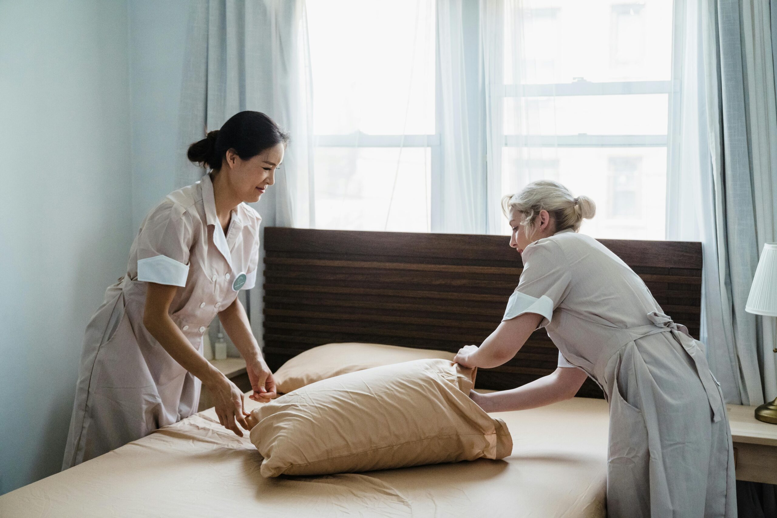 Two professional maids making a bed together in a bright, tidy room—highlighting the importance of choosing the best maid agency in Singapore.